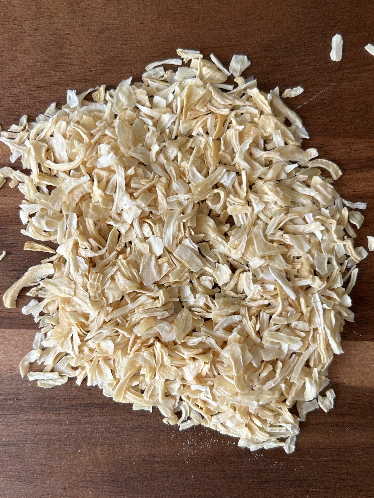 A pile of light‑yellow smoked onion flakes on a wooden surface, used by vegan chefs for gourmet Maas BBQ and other plant‑based recipes.