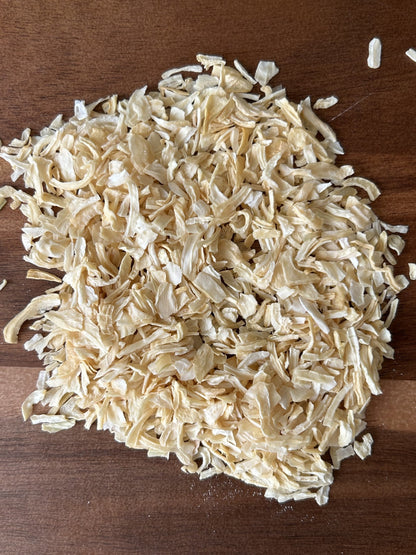 A pile of light‑yellow smoked onion flakes on a wooden surface, used by vegan chefs for gourmet Maas BBQ and other plant‑based recipes.
