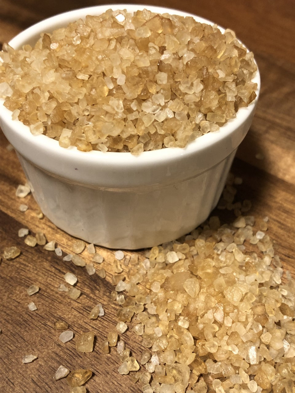 A white ramekin overflowing with golden Maas BBQ Smoked Sea Salt granules on a wooden surface, with some salt crystals scattered around. This high‑end, unique gourmet smoked sea salt, made in Alberta, Canada, is perfect for chefs and foodies for cooking, finishing dishes, and enhancing BBQ recipes, making it a great executive gift. Maas BBQ Smoked Sea Salt – High‑End Gourmet Finishing Salt, Unique Alberta‑Made Flavor for Chefs, Foodies & Executive Gifts