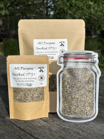All-purpose smoked SPG+ seasoning blend made with salt, pepper, and garlic, shown in a glass jar and brown paper packaging on a wooden surface.
