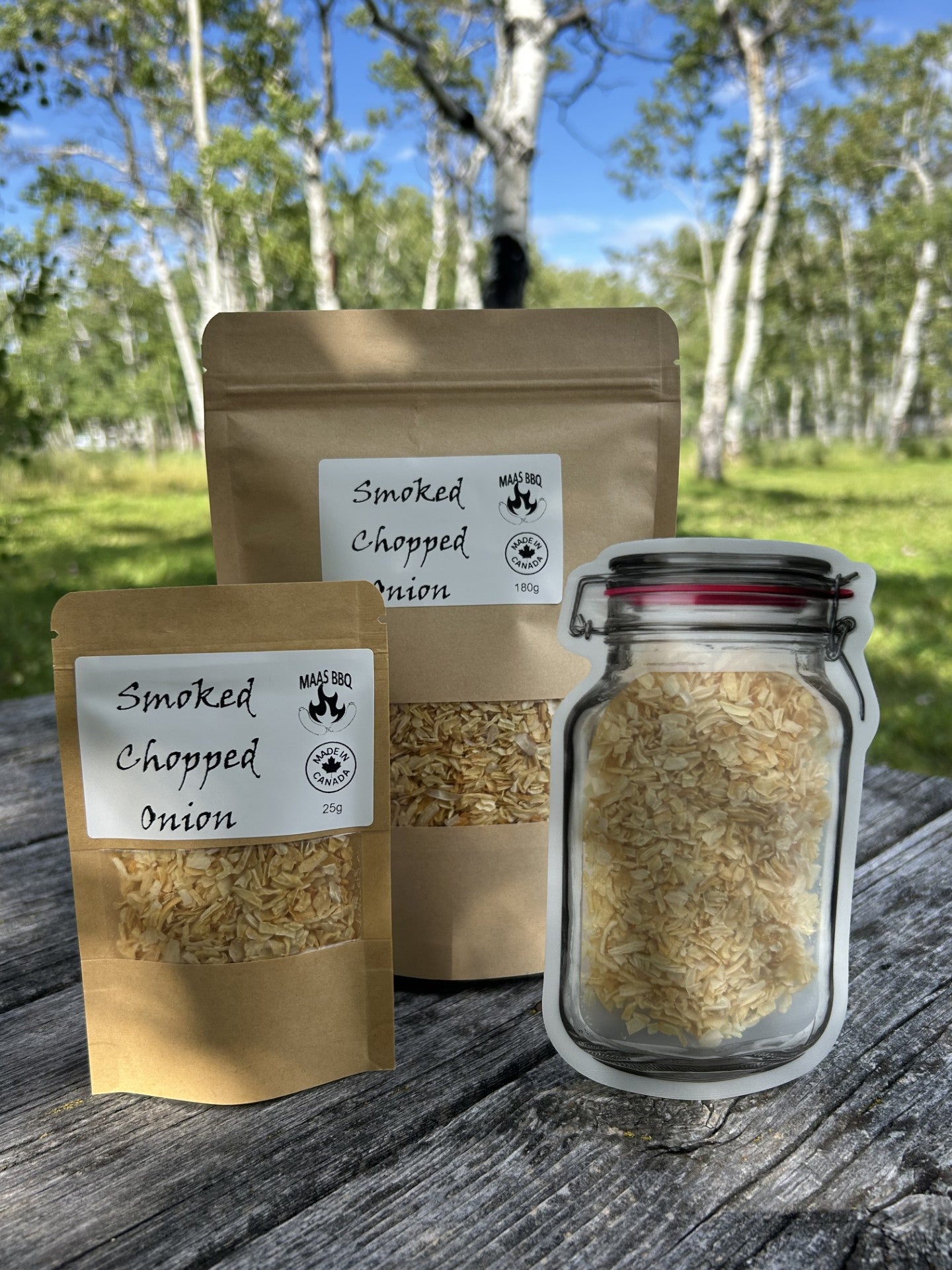 Three containers of Maas BBQ smoked chopped onion flakes on a rustic wooden table outdoors among trees; a small brown pouch (25g), a large brown pouch (180g), and a mason jar filled with golden vegan smoked onion flakes, labeled “Smoked Chopped Onion,” suitable for gourmet plant‑based chef recipes and BBQ flavoring.
Culinary tags: #MaasBBQ #smokedonionflakes #vegan #plantbased #gourmet #chef #BBQ #seasoning #flakes #culinary #onion #smoked #foodie #flavor #cook #veganchef #gourmetcooking #plantbasedchef #sm