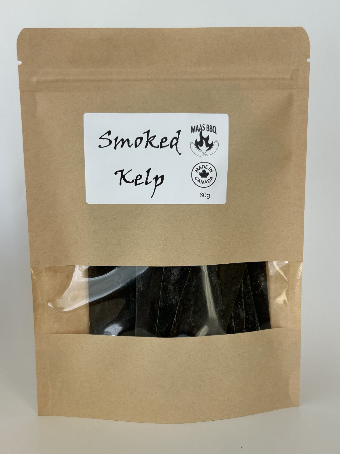 A brown resealable pouch with a white label reading “Smoked Kelp” and the Maas BBQ logo (“MAAS BBQ” with a flame emblem and “Made in Canada 60g” stamp). The pouch has a clear window showing dark smoked kelp strips inside.
Culinary tags: #MaasBBQ #smokedkelp #vegan #plantbased #gourmet #chef #snack #Canadianfood #BBQ #seaweed