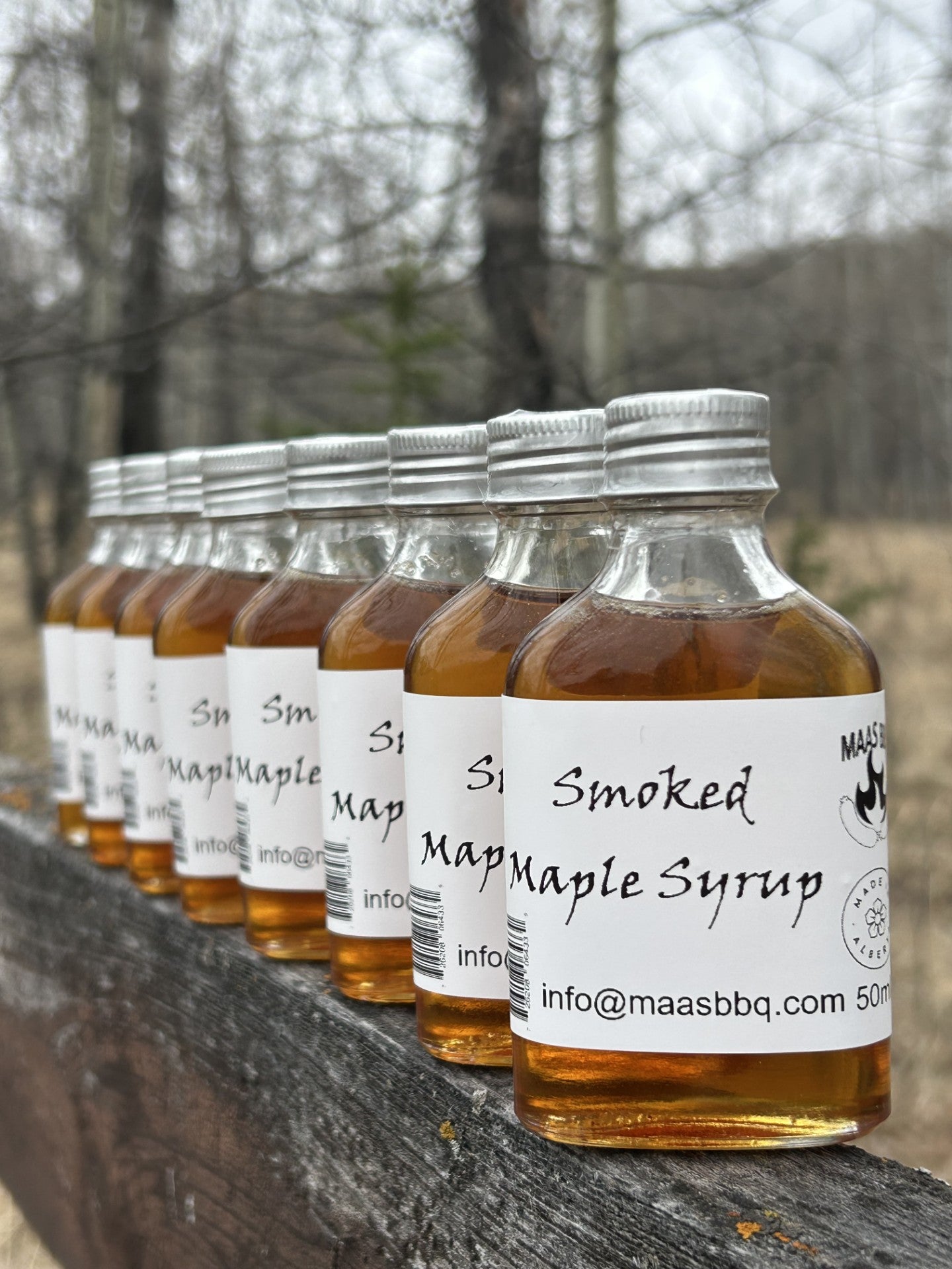 Row of bottles of smoked maple syrup with labels on a wooden surface.