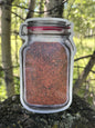 Clear jar with red lid containing a spice mix on a tree stump with a forest background